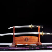Two Japanese swords on a wooden stand with a black background